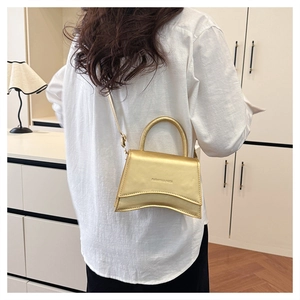 Détail du mini sac sablier doré métallisé avec base incurvée porté par un mannequin en blanc