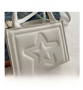Detail shot of a white square handbag featuring a prominent raised star pattern and gold hardware