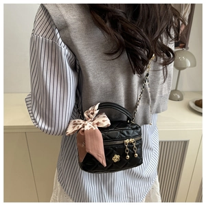 Detail of black quilted mini bag featuring golden camellia charm and silk scarf handle