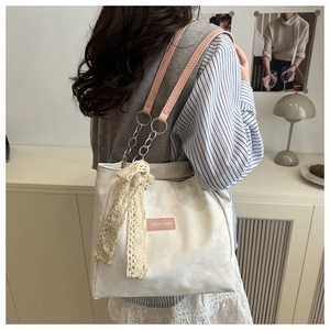 Détail d'un sac cabas blanc avec bandoulières roses, chaîne et nœud en dentelle