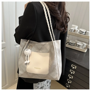 Detail of woven handles and plush charm on a large gray tote bag with Fashion slogan