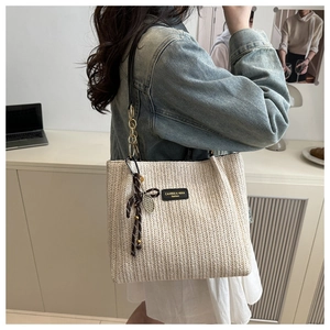 Dettaglio della borsa in paglia beige con trama a spina di pesce e ciondolo