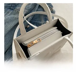 Detail view of smooth metal zipper and black interior of the white square crossbody bag