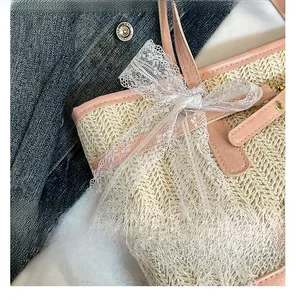 Close-up of woven straw tote bag with white lace bow and pink leather trim details