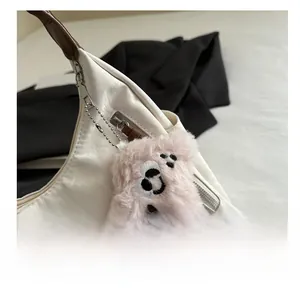 Dettaglio di un ciondolo a forma di orsetto rosa con catena di metallo su borsa bianca