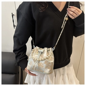 Detail view of light blue embroidered bucket bag with gold floral motifs and pearl handle