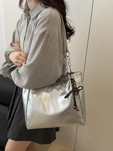 Silberne Metallic-Tragetasche mit Schleife und Kettenriemen am Modell getragen