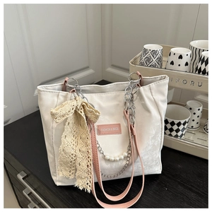 Détail du sac fourre-tout beige avec bandoulière rose, chaîne de perles et nœud