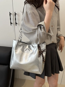 Silberne Tote Bag mit Schleifen-Detail und Kettenriemen, präsentiert an einem Model