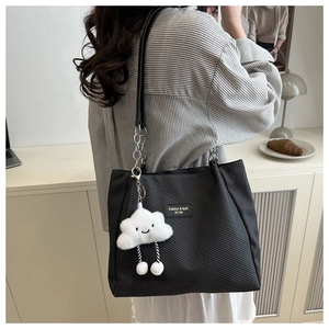Detail of black tote bag featuring twill texture, chain strap, and plush cloud charm