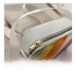 Close-up of smooth gold-tone zipper and rainbow metallic stripes on white pebbled leather bag