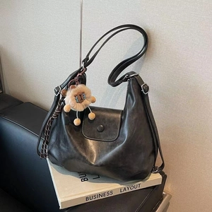 Detail of dark grey vintage hobo bag with lion pendant on a business book and sofa
