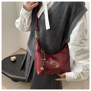 Détail du sac bandoulière rouge foncé avec lettres dorées et pendentif cloche tressé