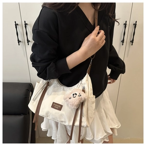 Dettaglio della borsa tote crema con zip laterali e ciondolo a forma di orsetto di peluche