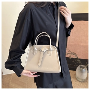 Detail view of a cream leather handbag with metallic buckle on a black dress model