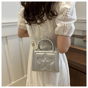 Close-up of silver square bag with embossed star detail worn by model as a crossbody