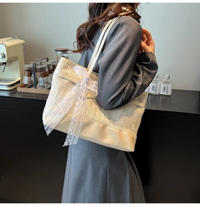 Detail of a beige woven tote bag featuring a white lace bow on the side for summer