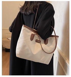 Close-up of off-white tote bag with brown leather handles worn by a model in daily style