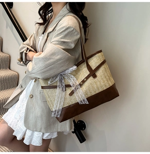 Detail view of woven straw tote bag featuring leather trim and large white lace bow