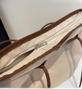 Detailed close-up of smooth metal zipper closure on large beige tote bag with brown trim