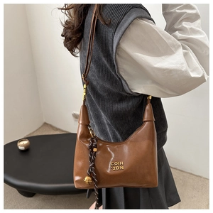 Sac croissant en cuir marron avec logo doré et breloque tressée porté par un modèle