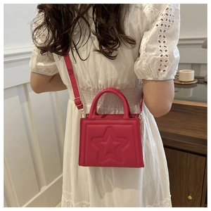 Detail of rose red crossbody bag with embossed star pattern worn on white dress
