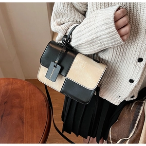 Detail of color-block crossbody bag with knotted handle and fashion tag on beige sweater