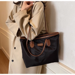 Detail einer schwarzen Nylon-Tragetasche mit braunem Ledergriff getragen zum beigen Mantel