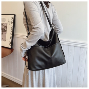 Side view of a large black pebbled leather tote bag with slim straps and side pockets