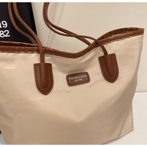 Detailansicht der beigen Nylon-Tragetasche mit braunem Kunstlederbesatz und Logo-Schild