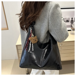 Nahaufnahme einer schwarzen glänzenden Hobo-Tasche mit Bärenanhänger an der Schulter