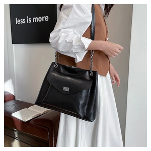 Detail of black leather chain tote bag with silver metal buckle on a shoulder model