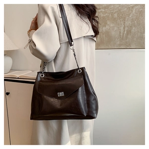 Detail of dark brown tote bag featuring glossy texture and metallic chain shoulder strap
