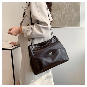 Detail of dark brown leather tote bag featuring a silver metal lock and chain strap