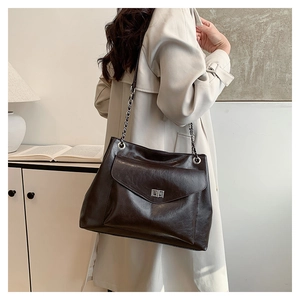 Detail of dark brown leather tote bag with silver chain strap worn with a beige trench coat