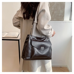 Detail of dark brown tote bag with metal turn-lock and chain strap on shoulder