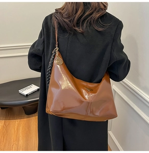 Detail of glossy brown leather hobo bag with tennis racket charm and metal plaque