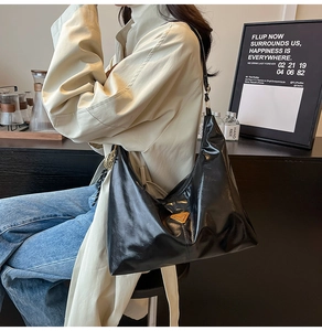Detail of glossy black leather hobo bag with golden triangle logo on beige coat