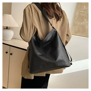 Detail view of large black tote bag with pleated leather texture on model shoulder