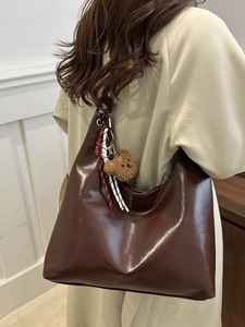 Braune glänzende Tragetasche im Retro-Stil mit Bärenanhänger an einem Model gezeigt