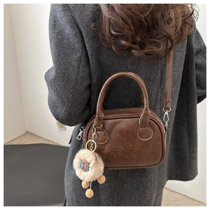 Detail der dunkelbraunen Handtasche mit Lucky OHIO Druck und beigem Plüsch-Anhänger