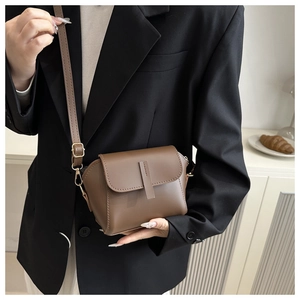 Detailed view of a brown leather crossbody bag with adjustable strap worn on black blazer