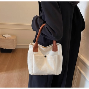 Detalle de bolso tote de lona blanco crema con asas marrones y bolsillo con botón clip