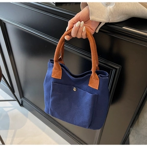Detalle del bolso de lona azul marino con asas de cuerda naranja y bolsillo con broche
