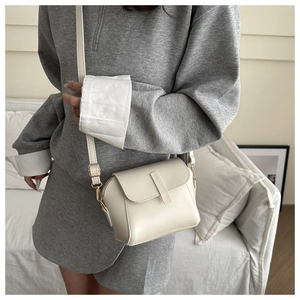 Close-up of a minimalist cream leather crossbody bag with adjustable strap and gold buckle