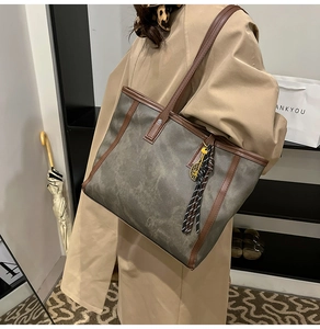 Große graue Tote Bag mit braunem Lederbesatz und Tennis-Anhänger in der Nahaufnahme