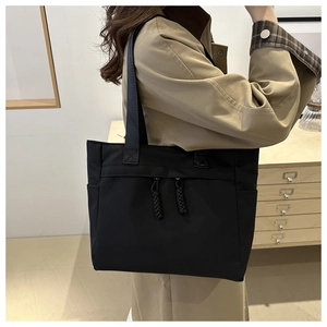 Detail of a large black tote bag showing side pockets and woven zipper pullers