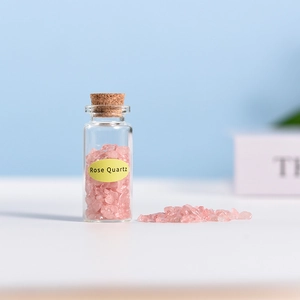 Mini glass bottle with cork filled with natural Rose Quartz crystals on a blue background