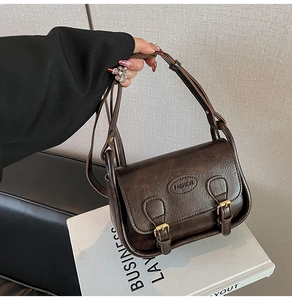 Detail of dark brown vintage faux leather shoulder bag with gold buckle and fashion logo