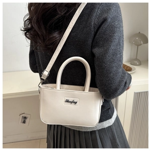 Detail of cream white leather crossbody square bag with silver logo plaque on gray outfit